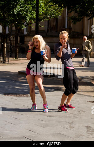 Dundee, Tayside, Scotland, UK. August 16th 2016: UK Weather. August heatwave sweeping across Tayside today with maximum temperature 27 °C. Although the schools in Scotland have re-opened others are enjoying the glorious warm sunshine in the city centre. Two fit athletic women wearing sportswear holding their cups of coffee pause for a photograph along Dundee High Street. Credit: Dundee Photographics / Alamy Live News Stock Photo