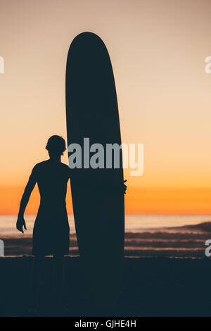 Silhouette of Man standing on beach at sunset holding surfboard, San Diego, California, United States Stock Photo