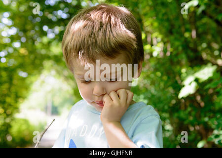 Boy standing in garden with hand on chin Stock Photo