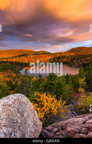 The Bowl surrounded by fall color with Cadillac Mountain in the background at sunrise in Acadia National Park, Maine.