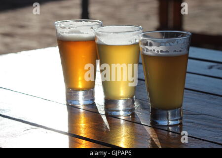 A selection of three craft beers during a tasting session on a wooden table with the sun shining into the glasses Stock Photo