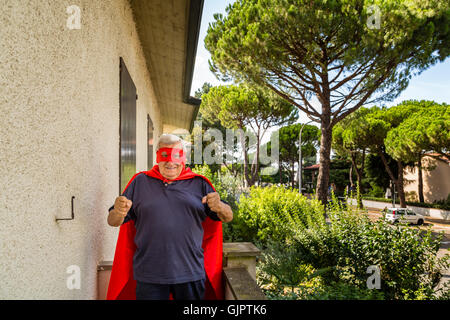 an old man dressed as a superhero on balcony of his house showing fists Stock Photo