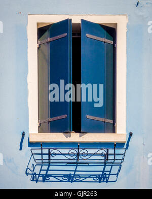 Dark blue partially opened window shutters on a pale blue rendered exterior wall of traditional house on the island of Burano. Italy. Stock Photo