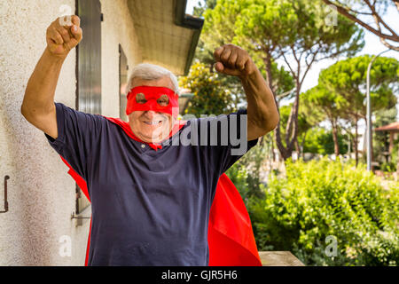 an old man dressed as a superhero on balcony of his house showing fists Stock Photo