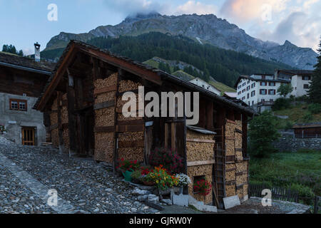 View on an old wooden house with neatly stacked firewood in front in the town of Splugen in Switzerland. Stock Photo