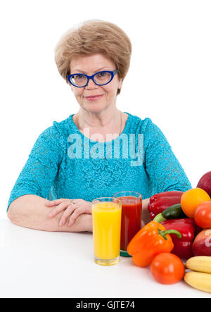 Woman retirement age with tomato and orange juice in glasses sits at table with fruits and vegetables, isolated on white backgro Stock Photo