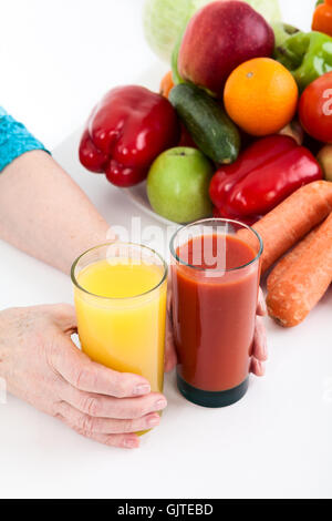 Fresh fruits and vegetables are on table next to female hands with glasses of tomato and orange juices Stock Photo