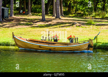 Old wooden motorboat moored by the shore with pine trees and grass in the background. Stock Photo