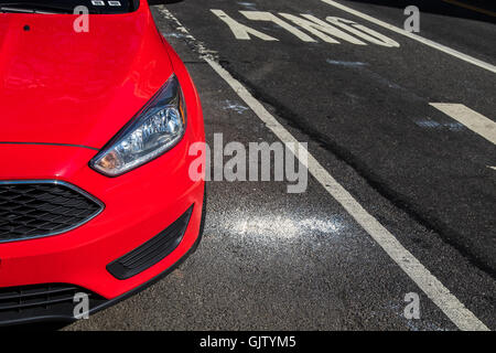 A partial view of a new red car parked in the street. Stock Photo