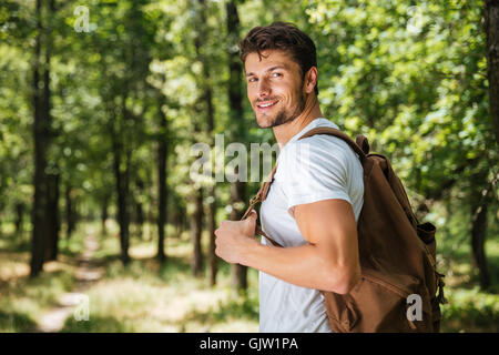 Happy young man with backpack walking in forest Stock Photo