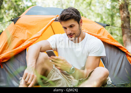Serious young man tourist using mobile phone in toristic tent at forest Stock Photo