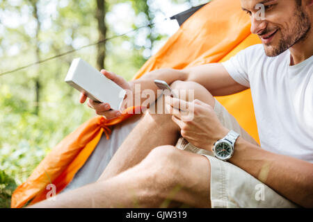 Smiling young man tourist using mobile phone and portable mini speaker in forest Stock Photo