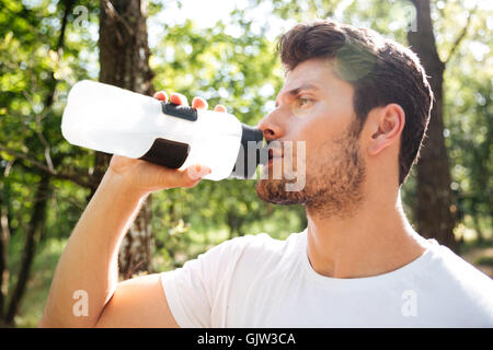 Portrait of attractive young sportsman standing and drinking water outdoors Stock Photo
