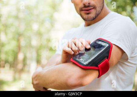 Closeup of young man athlete using mobile phone in handband outdoors in the morning Stock Photo