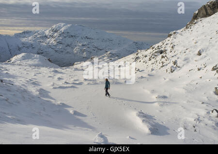 A solo mountaineer walks across a frozen lake on the summits of mountains in the Scottish Highlands in winter. Stock Photo