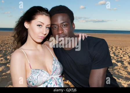 Attractive  Couple  multicultural mixed race  head and shoulders heads together looking serious on beach  romantic Stock Photo