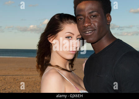 Young couple multicultural mixed race head and shoulders heads together looking  into camera on beach  romantic love romance Stock Photo