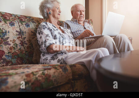 Indoor shot of elderly couple relaxing on a couch with a laptop computer. Senior man and woman relaxing on a sofa using laptop. Stock Photo