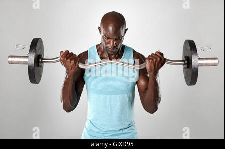 Portrait of a muscular man lifting barbell against grey background. African fitness model working out with weights. Stock Photo