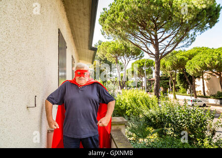 an old man dressed as a superhero on balcony of his house showing fists Stock Photo