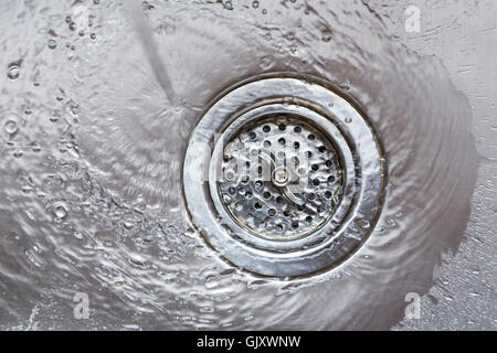 Water flowing going down drain in stainless steel kitchen sink wasting natural resources Stock Photo