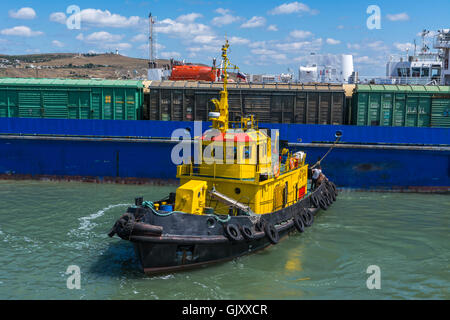 Yellow tugboat assisting large cargo ship Stock Photo