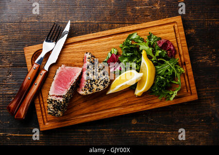 Grilled Tuna steak in sesame and lemon on wooden board on dark wooden background Stock Photo