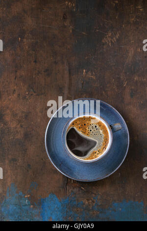 Blue ceramic cup of black hot coffee on saucer, served over old wooden textured background. Simple minimalist style. Top view. C Stock Photo