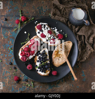 Set of dessert sandwiches with fresh berries blueberry and raspberry, cream cheese, thyme and honey, served with jug of milk on Stock Photo