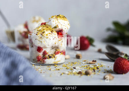 A couple scoops of coconut milk and cashew ice cream topped off with strawberries and pistachio crumbs is photographed from the Stock Photo