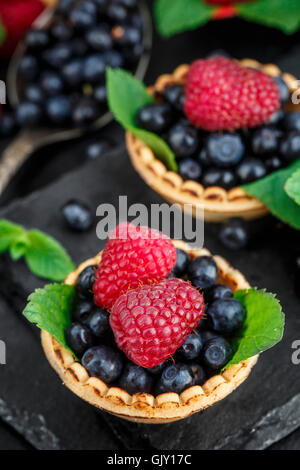 Tartlets with blueberries, raspberries and mint leafs on a black slate background Stock Photo