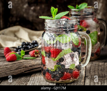 Detox drink with fresh berries, mint and ice in glass jars on wooden background Stock Photo