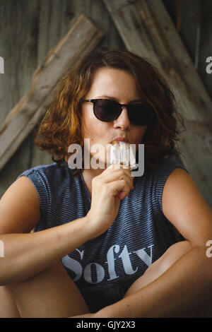 Tanned girl eating popsiclesitting in front of the wooden door Stock Photo