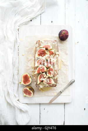 Loaf cake with figs, almond and white chocolate sauce on white serving board over white wooden background, top view Stock Photo
