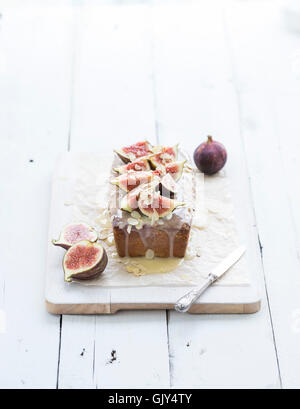 Loaf cake with figs, almond and white chocolate on white serving board over white wooden background, selective focus Stock Photo