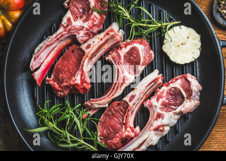 Raw uncooked lamb meat chops with rosemary and garlic in black iron grilling pan, top view, horizontal composition Stock Photo