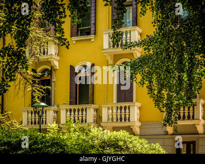 Traditional yellow-rendered building with shutters and Venetian blinds at the arched windows. Venice, Italy. Stock Photo