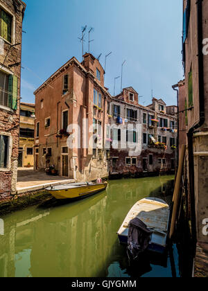 Moored boats on a narrow canal with traditional buildings either side. Venice, Italy. Stock Photo