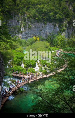 Tourists strolling on wooden walkways lined by petasites, along the Korana river (Plitvice Lakes National Park - Croatia). Stock Photo
