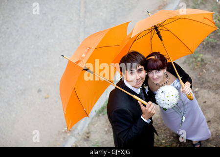 portrait of bride and groom with orange umbrellas Stock Photo