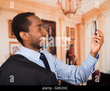 Headshot handsome man wearing business suit taking a selfie with mobile phone, as seen from profile angle, lobbby background Stock Photo