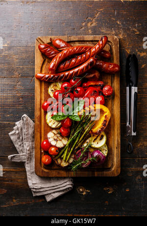 Grilled sausages and vegetables on cutting board on dark wooden background Stock Photo