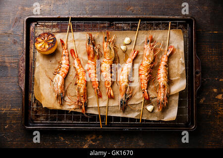 Grilled fried Tiger prawns shrimps on skewers and lemon on metal grid baking sheet background Stock Photo