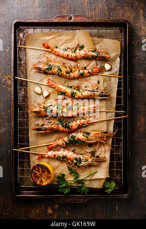 Grilled fried Tiger prawns shrimps on skewers with green sauce and lemon on metal grid baking sheet background Stock Photo