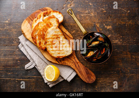 Mussels in copper pot, bread toasts and lemon on wooden background Stock Photo