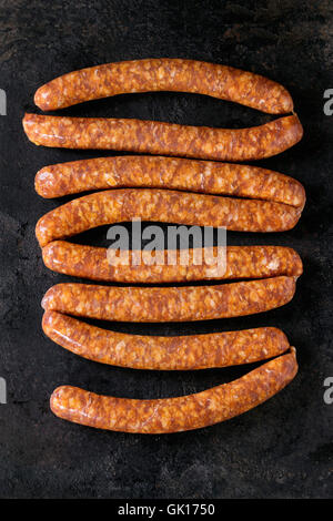 Fresh raw beef sausages with spices for BBQ over black iron textured background. Top view Stock Photo