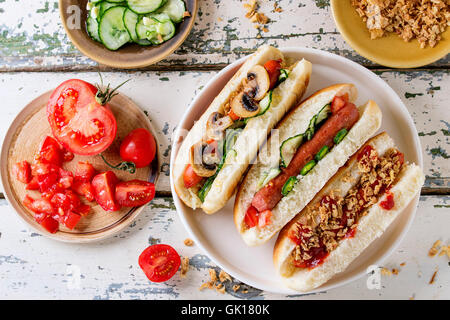 Assortment of homemade hot dogs with sausage, fried onion, tomatoes and cucumber, served with ingredients in big white plate ove Stock Photo