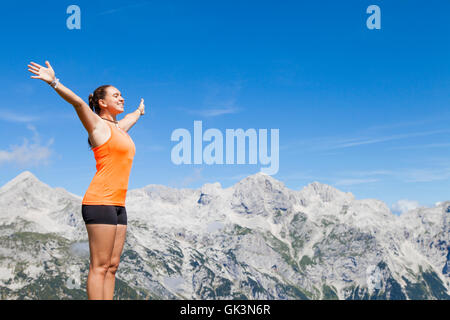 Pretty woman hiker standing on mountain rock with raised hands Stock Photo