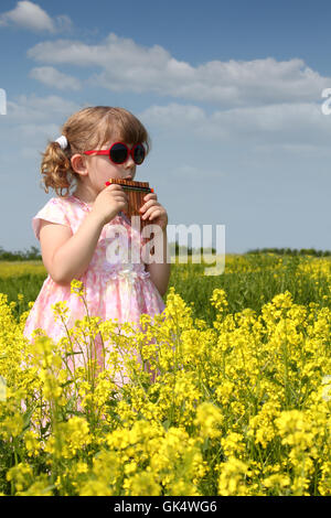 little girl standing in yellow flower field and play pan pipe Stock Photo