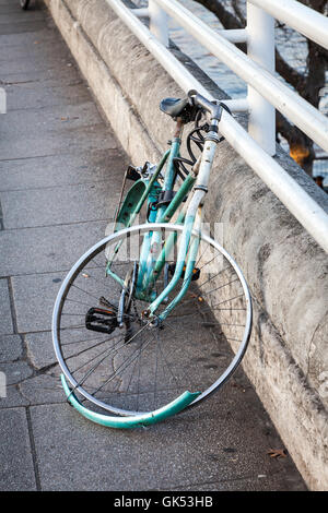 The remains of a bicycle which has been vandalized are still locked to the railings of a bridge Stock Photo